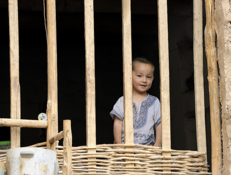 bambino uiguro sbircia i visitatori nella  cittadina di Tuyuk nello Xinjiang cinese