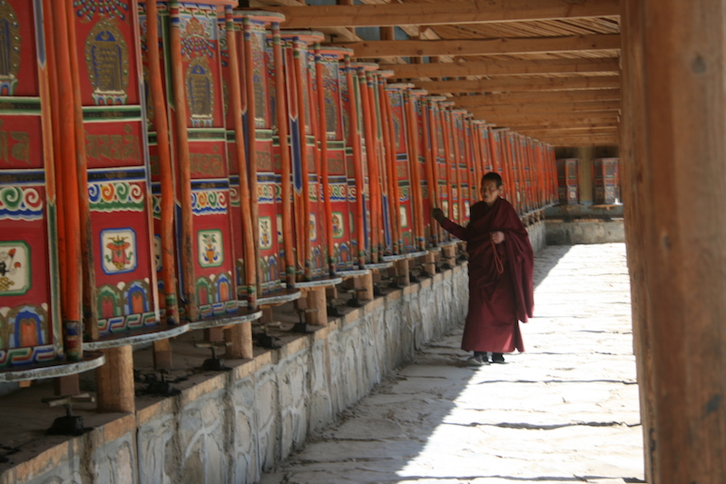 pellegrino cammina e recita la kora vicino alle ruote di preghiera  buddiste all'ingresso del Monastero di Labrang a  Xiahe in Cina